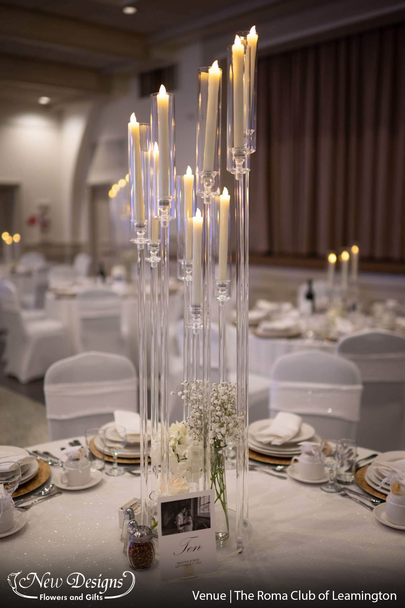 tall clear acrylic candleholders spiral upwards at gradually increasing heights, in a hall of crisp white linens and crystal candelabras